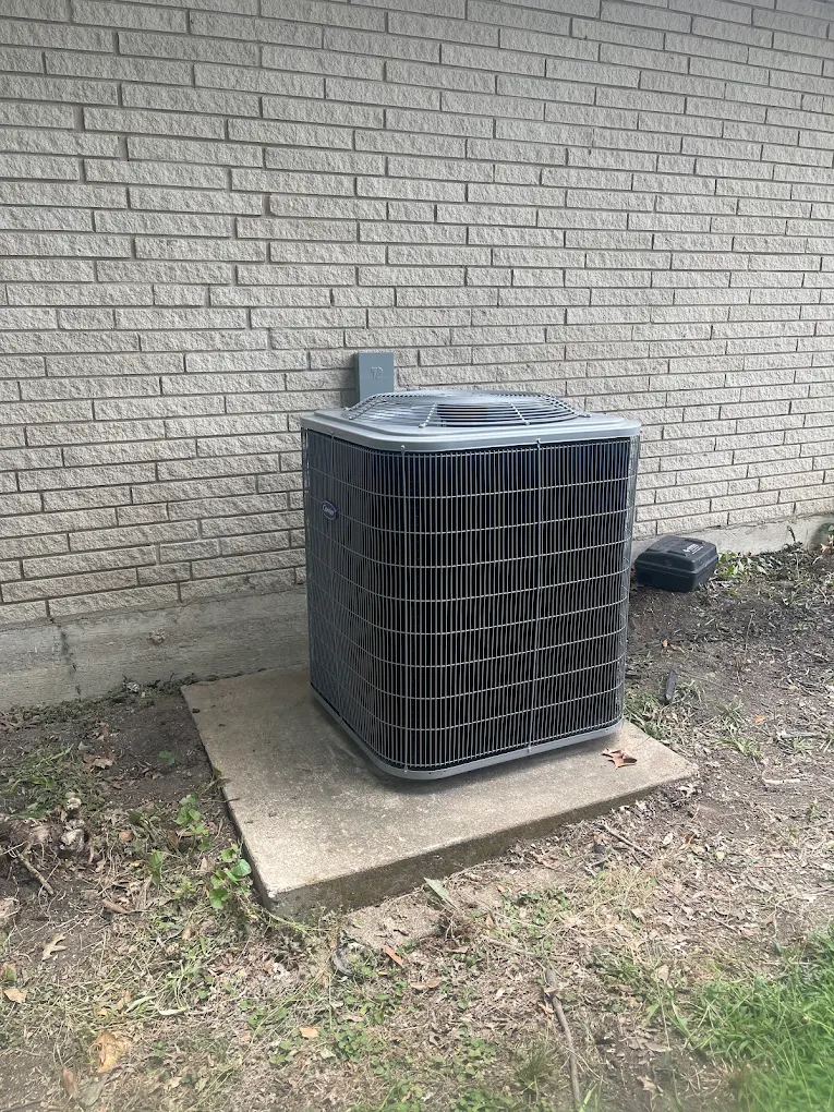 Newly installed Carrier air conditioner condenser on a concrete pad beside a brick home